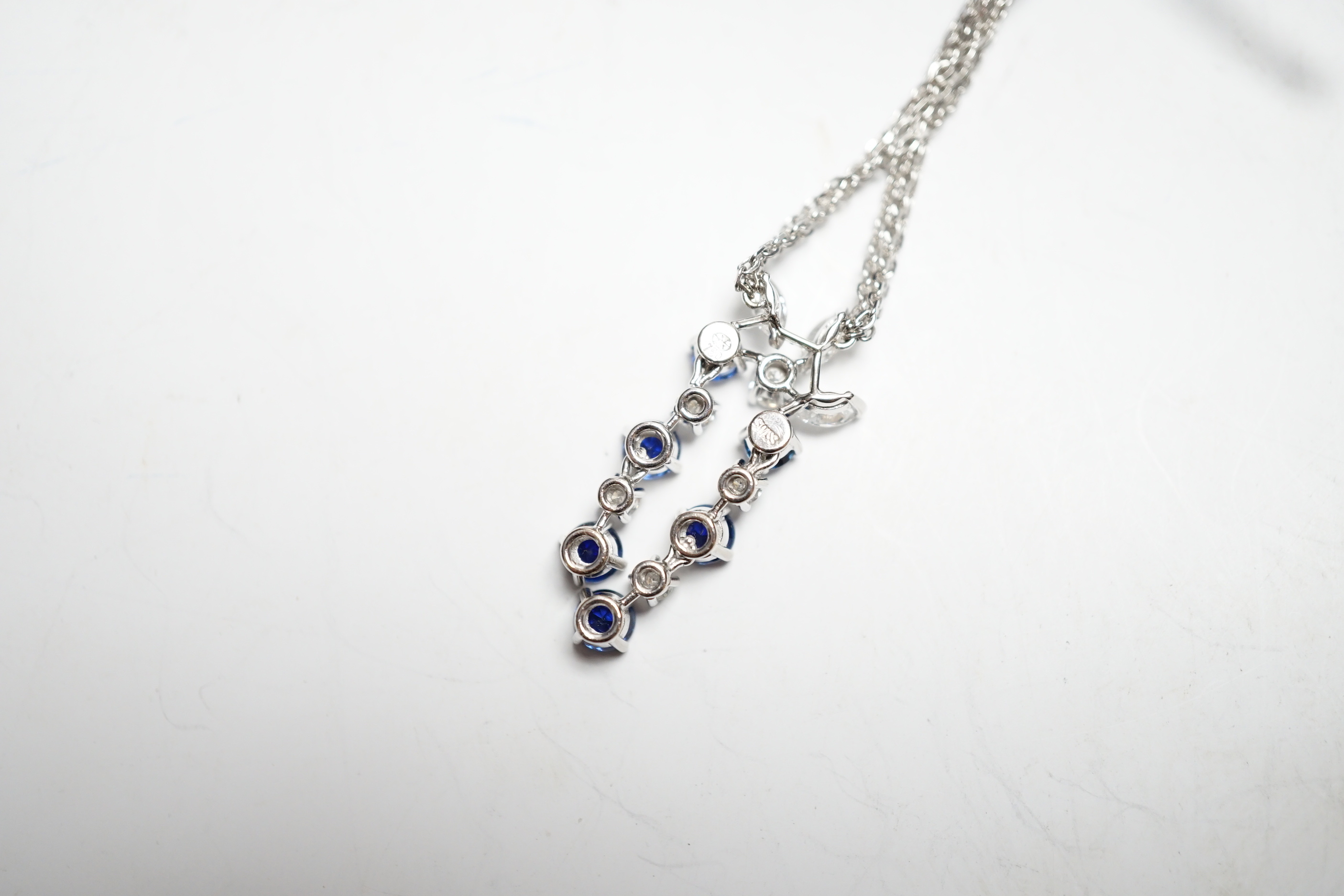 A modern 750 white metal, sapphire and diamond set cluster pendant, 31mm, on a twin strand white metal chain, 44cm, gross weight 10.3 grams, in a Bucherer box.